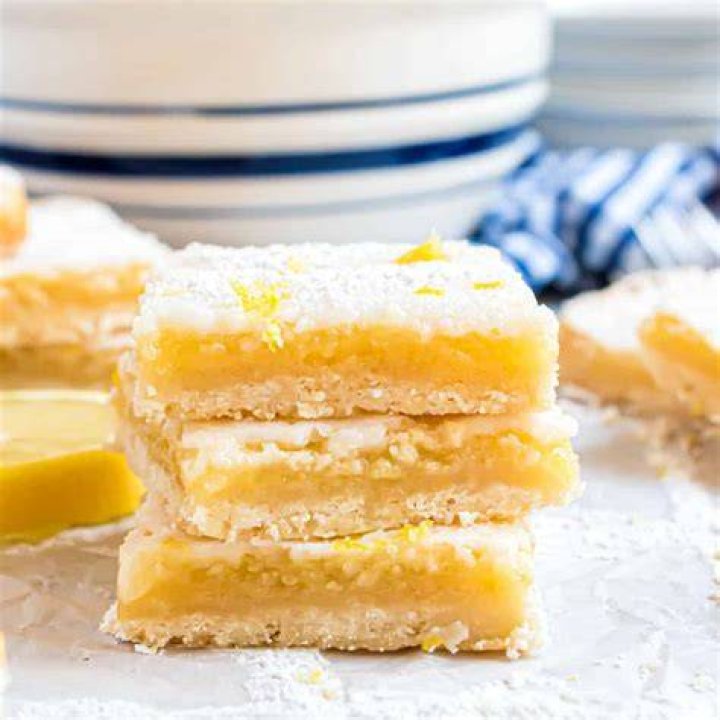 Lemon bars on a rack garnished with whipped cream and a lemon slice.